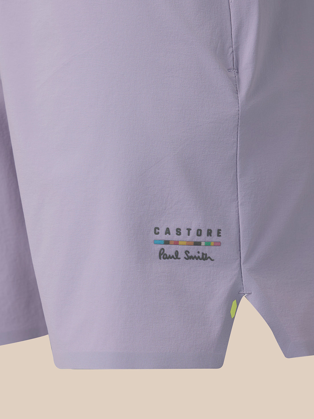Close-up of a light lavender shirt fabric showing the 'CASTORE' and 'Paul Smith' logo embroidery on the lower left side, with a small lime green button detail.