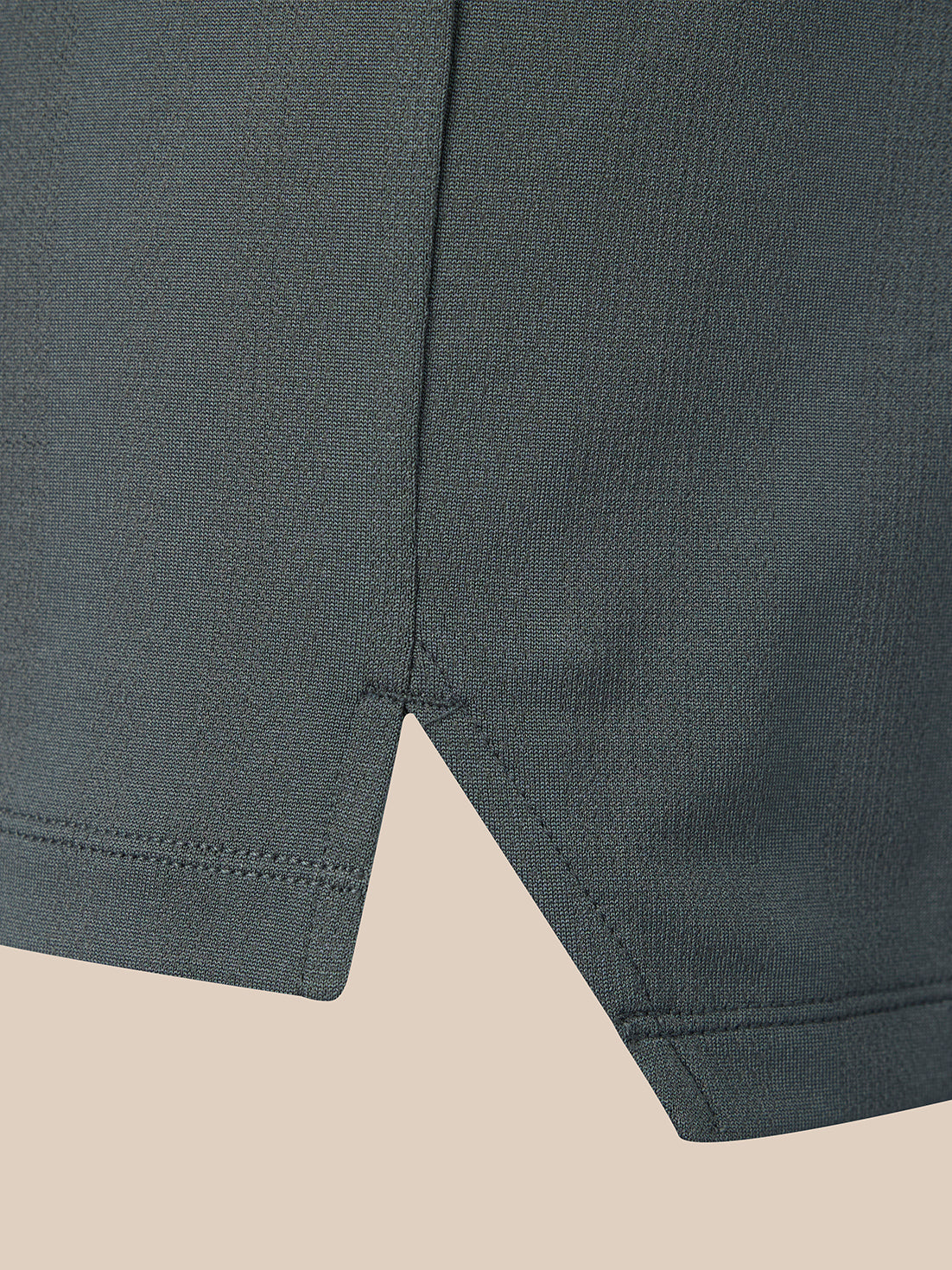 Close-up of a dark gray textured fabric garment showing a curved hem with a pointed V-shaped notch and neat stitching, set against a solid beige background.