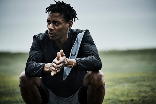 Athlete crouching on a rain soaked field with hands together, focused on training.