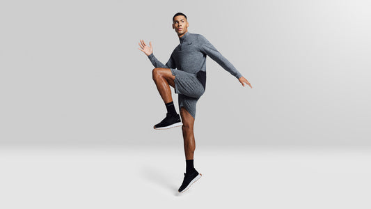 Male model in grey athletic outfit mid jump against a neutral studio backdrop