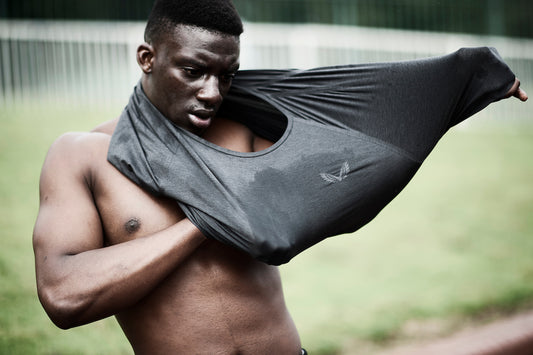 Man on a grassy field pulls a gray athletic shirt over his head.