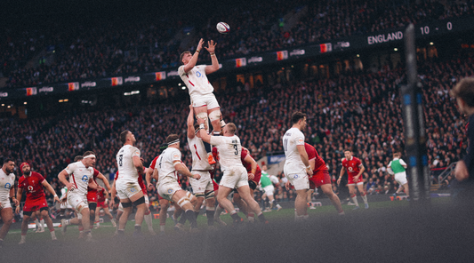 England rugby players in white jump for a ball in a lineout during a Six Nations match in a packed stadium.