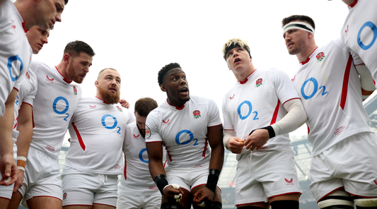 England rugby players in white jerseys form a huddle and listen during a team talk