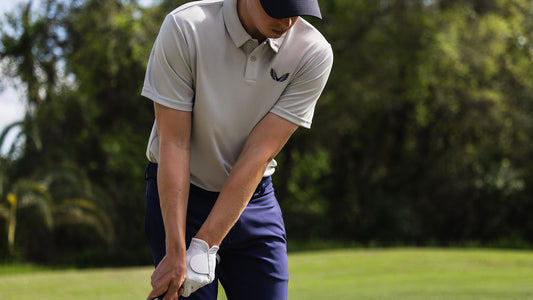 Golfer in a light gray polo and navy pants prepares to swing on a sunny golf course.