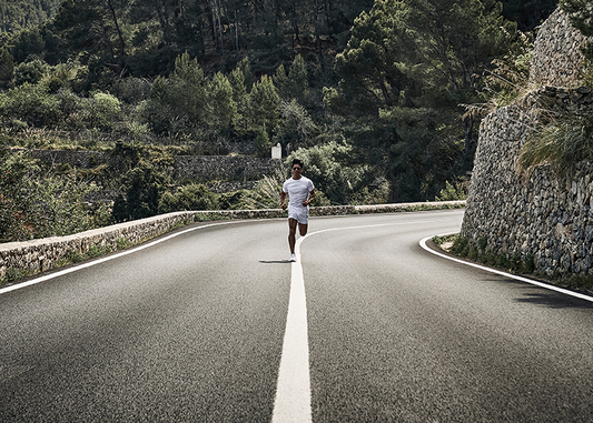 Runner jogging on a winding country road with stone walls and forested hills