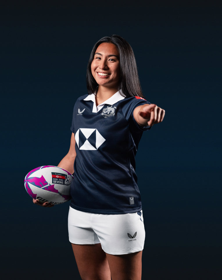 Woman in sports uniform holding a rugby ball against a dark background