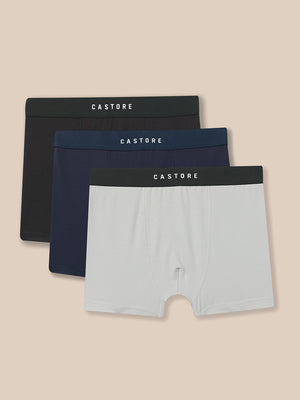 Three pairs of Castore men's boxer briefs in black, navy blue, and light gray, arranged in a stacked fan layout against a solid beige background.