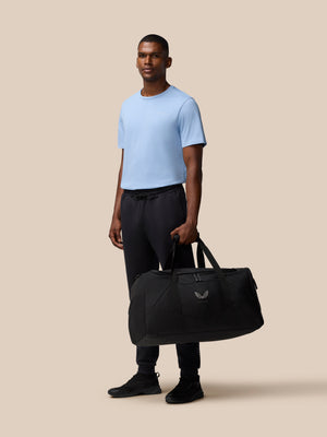 Man standing with a large black Core Holdall featuring padded handles and a detachable shoulder strap