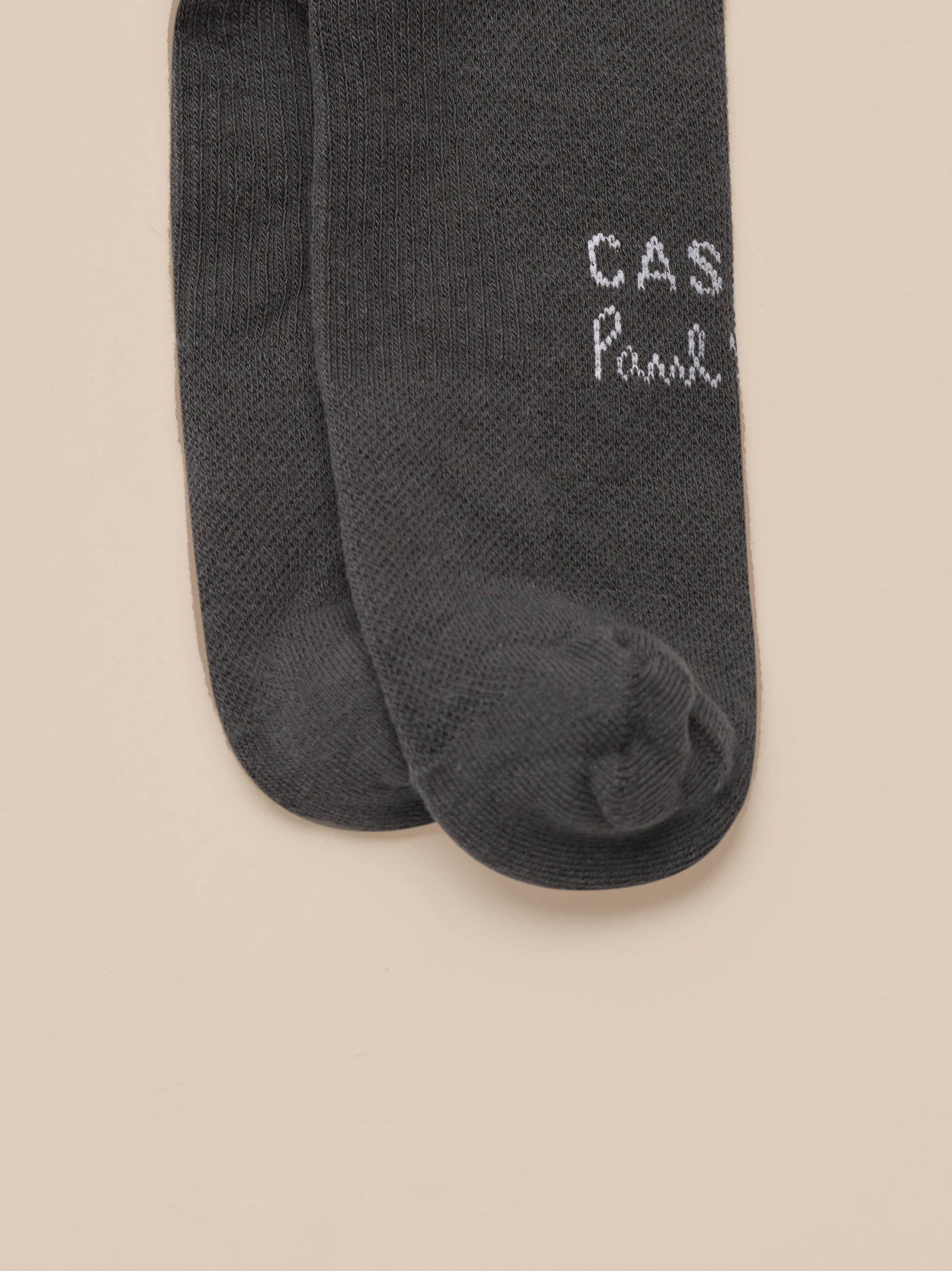 Dark gray socks with 'Castore Paul Smith' branding on a beige background