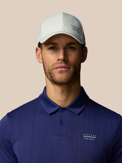 Man wearing a navy polo shirt and white cap with a brand logo on a beige background