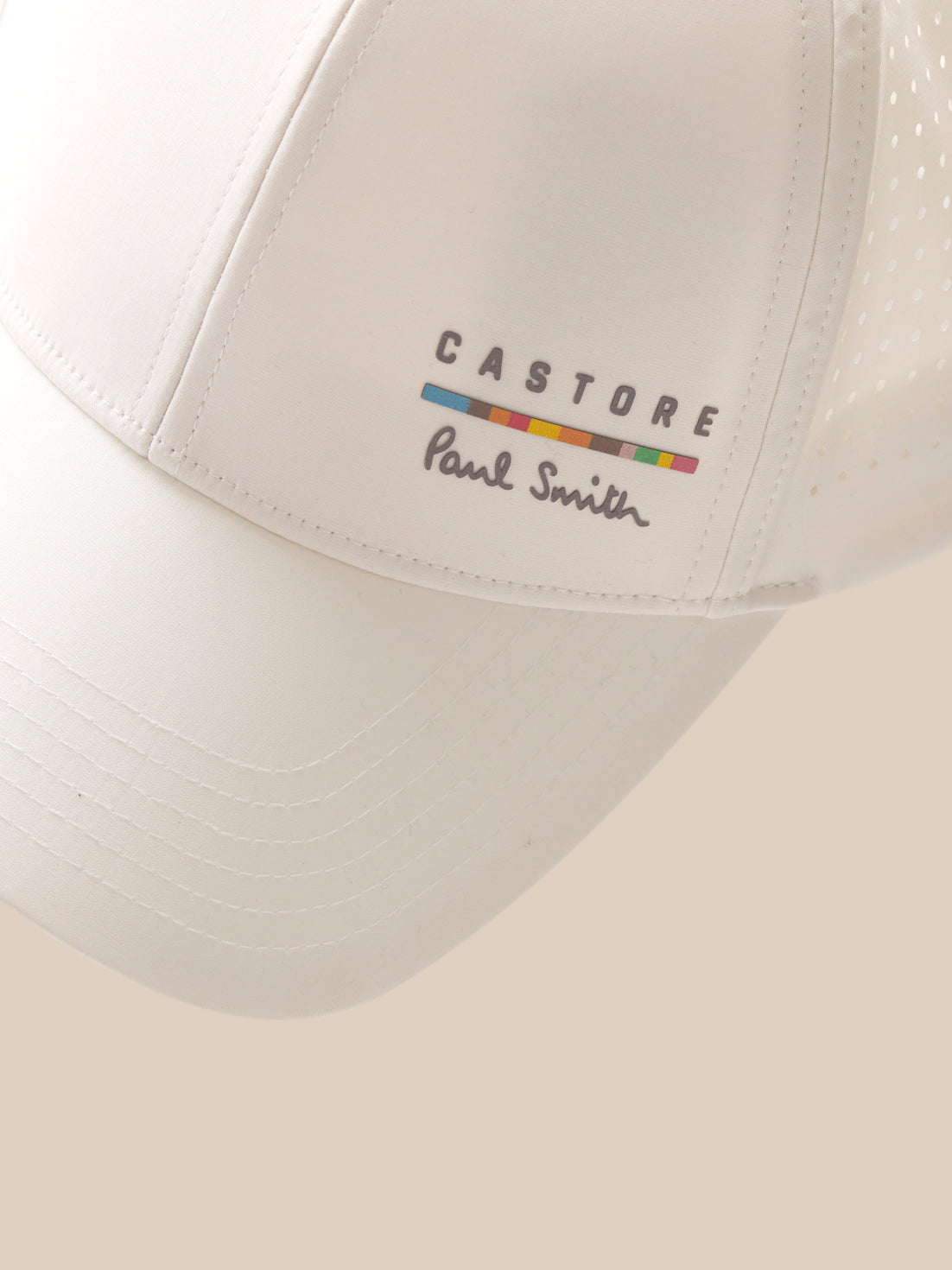 White cap with 'Castore Paul Smith' logo on a beige background