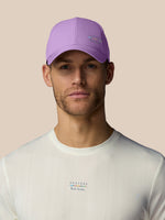 Man wearing a purple cap and white shirt with brand logos on a beige background