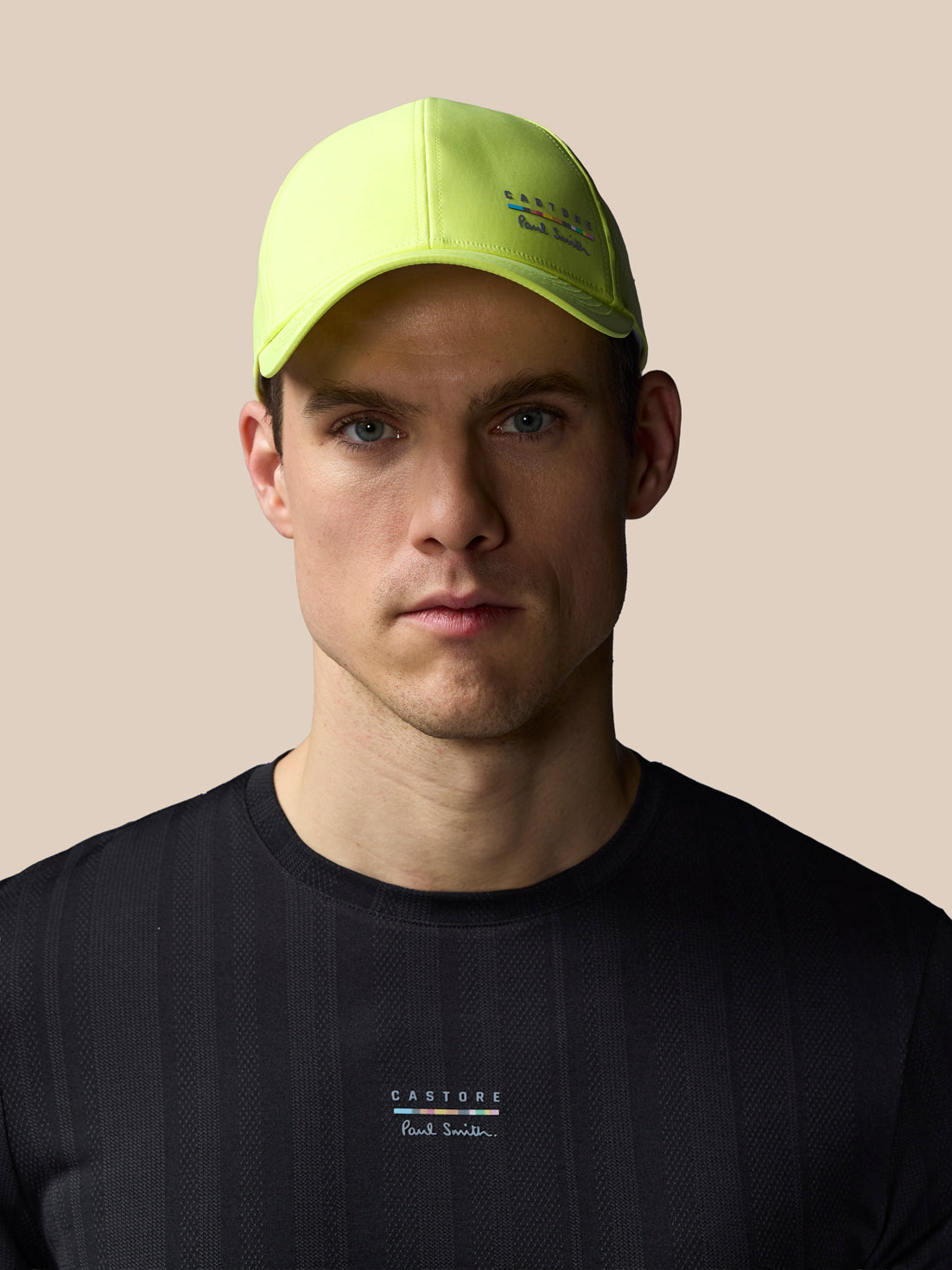Man wearing a bright yellow cap and black t-shirt with branding on a beige background