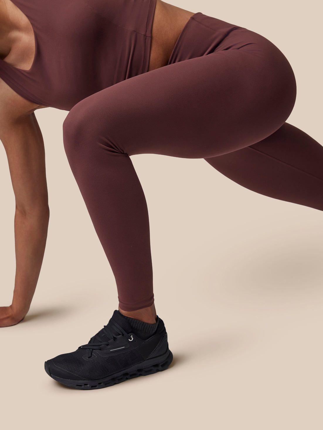 Person wearing maroon athletic leggings and black sneakers on a beige background