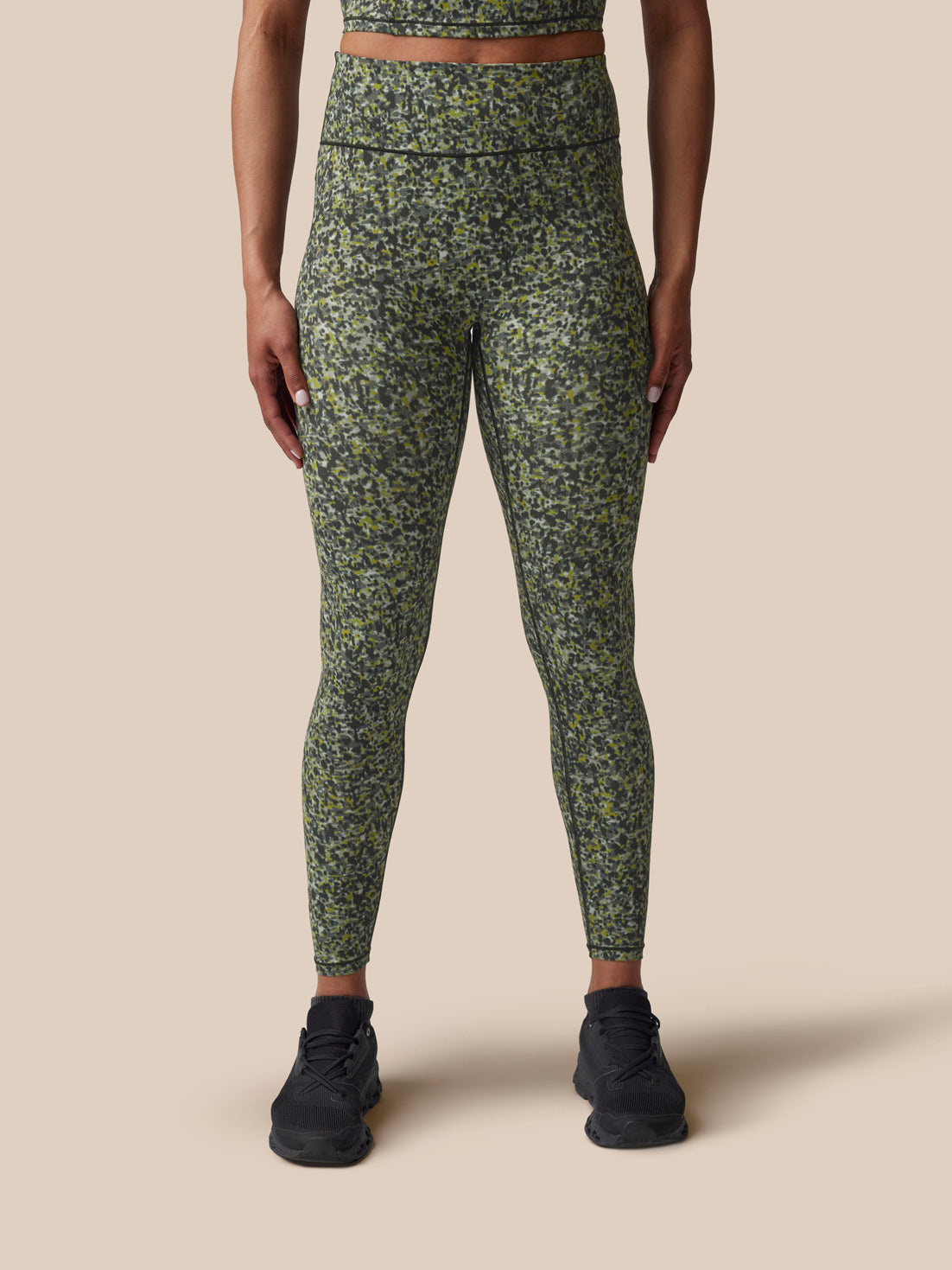 Person wearing green camouflage leggings on a beige background
