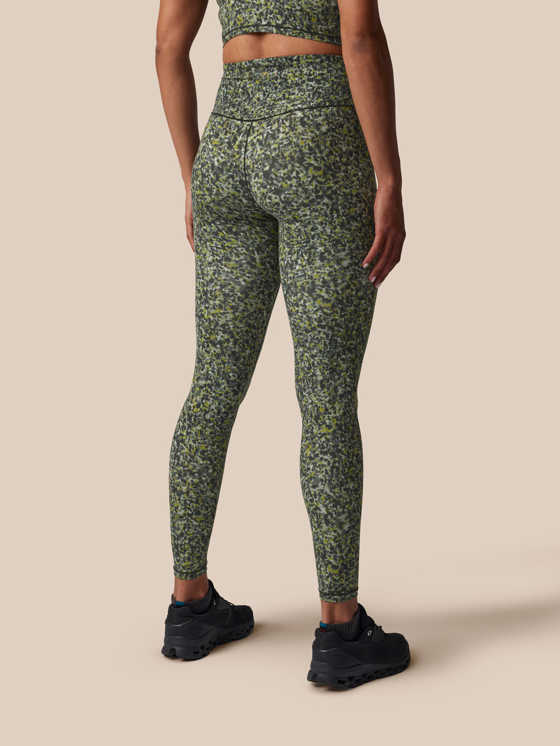 Person wearing green camouflage leggings on a beige background