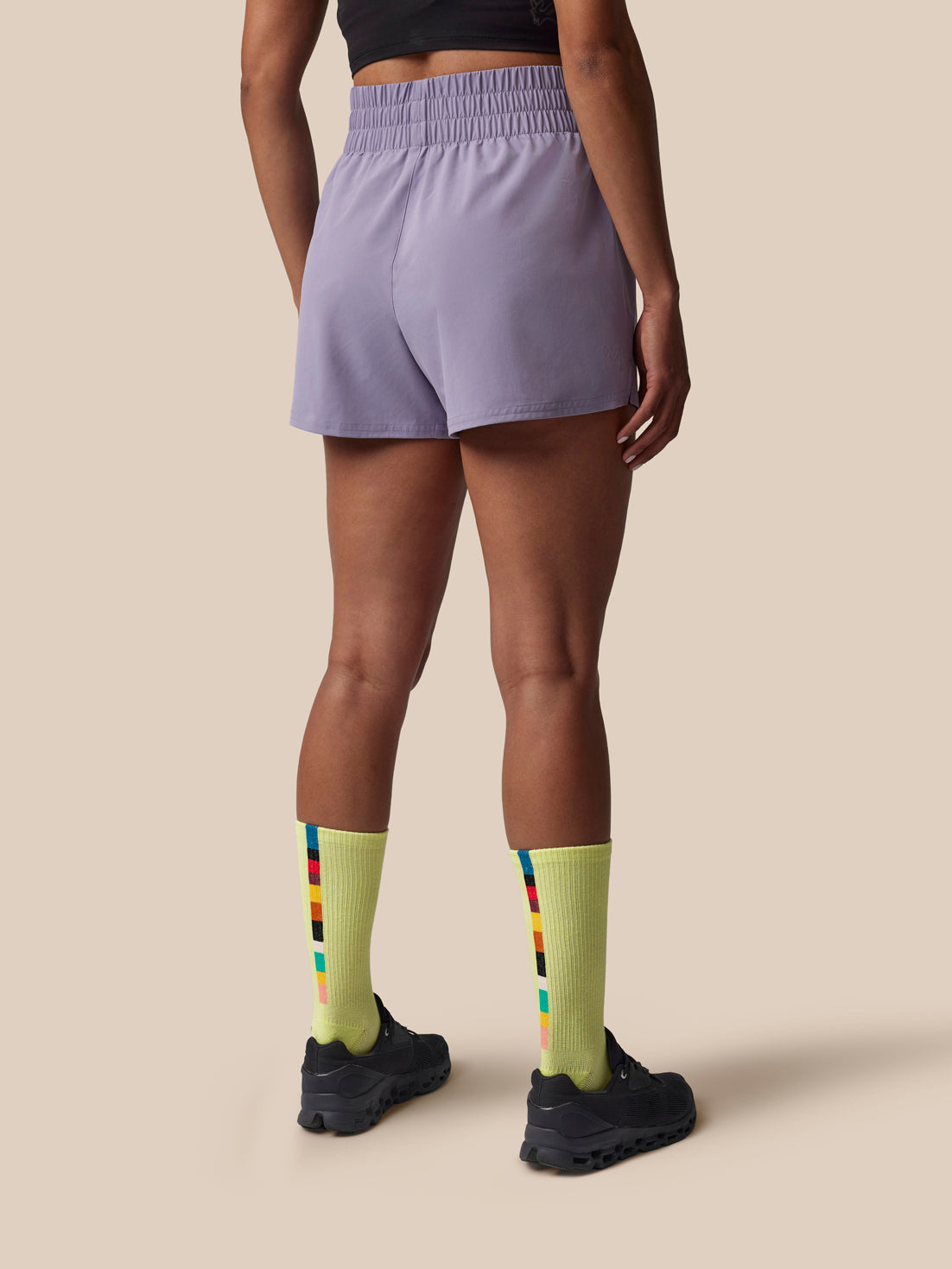 Person wearing light purple shorts and yellow socks with a colorful stripe on a beige background