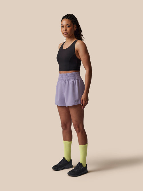 Woman wearing a black tank top, light purple shorts, and yellow socks on a beige background