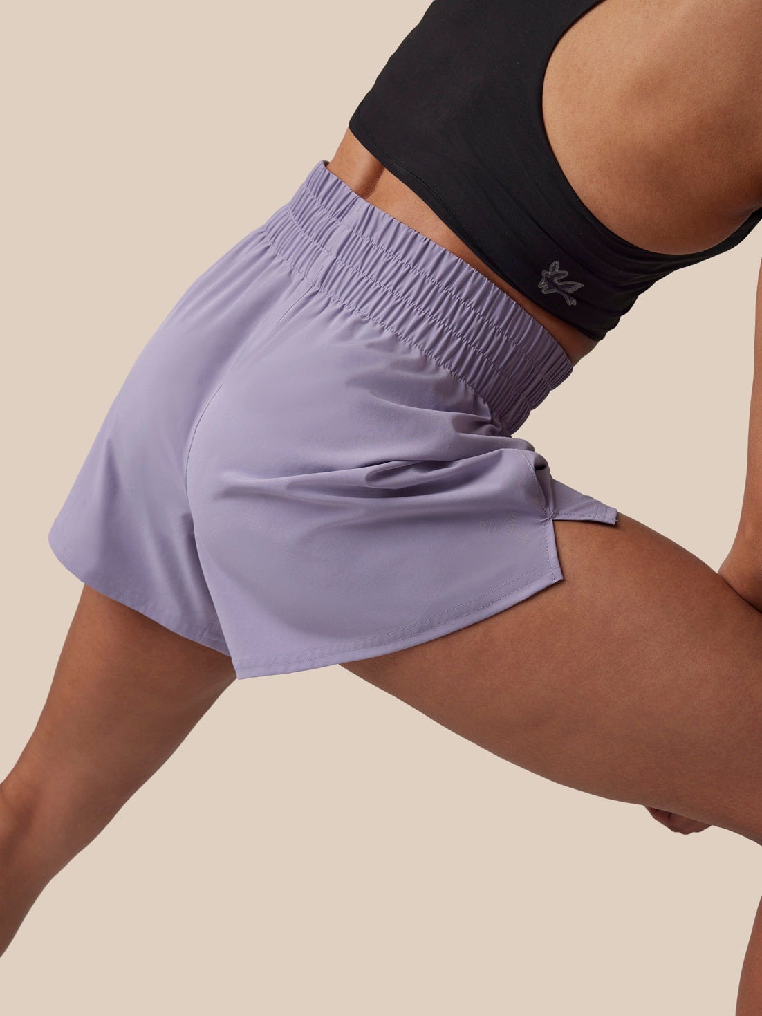 Person wearing light purple athletic shorts and a black sports bra on a beige background