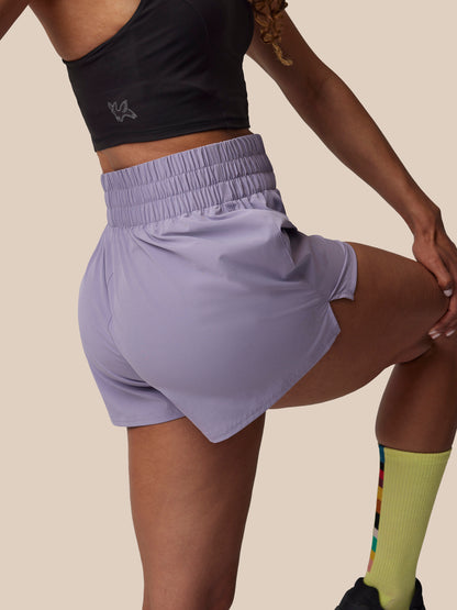 Person wearing a black crop top and light purple shorts on a beige background