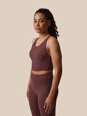 Woman wearing a brown sports bra and leggings set against a beige background