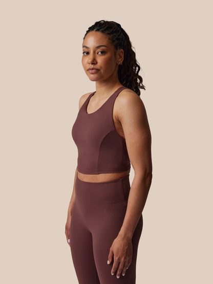 Woman wearing a brown sports bra and leggings set against a beige background