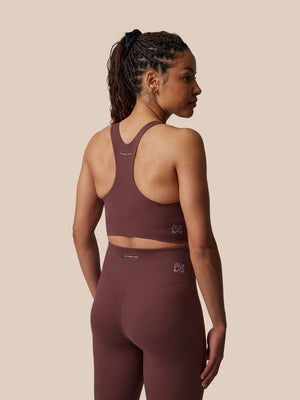 Woman wearing a maroon sports bra and leggings set on a beige background