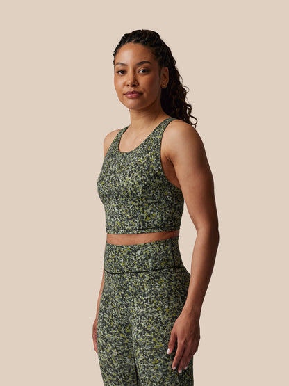 Woman wearing a green floral sports bra and leggings set against a beige background