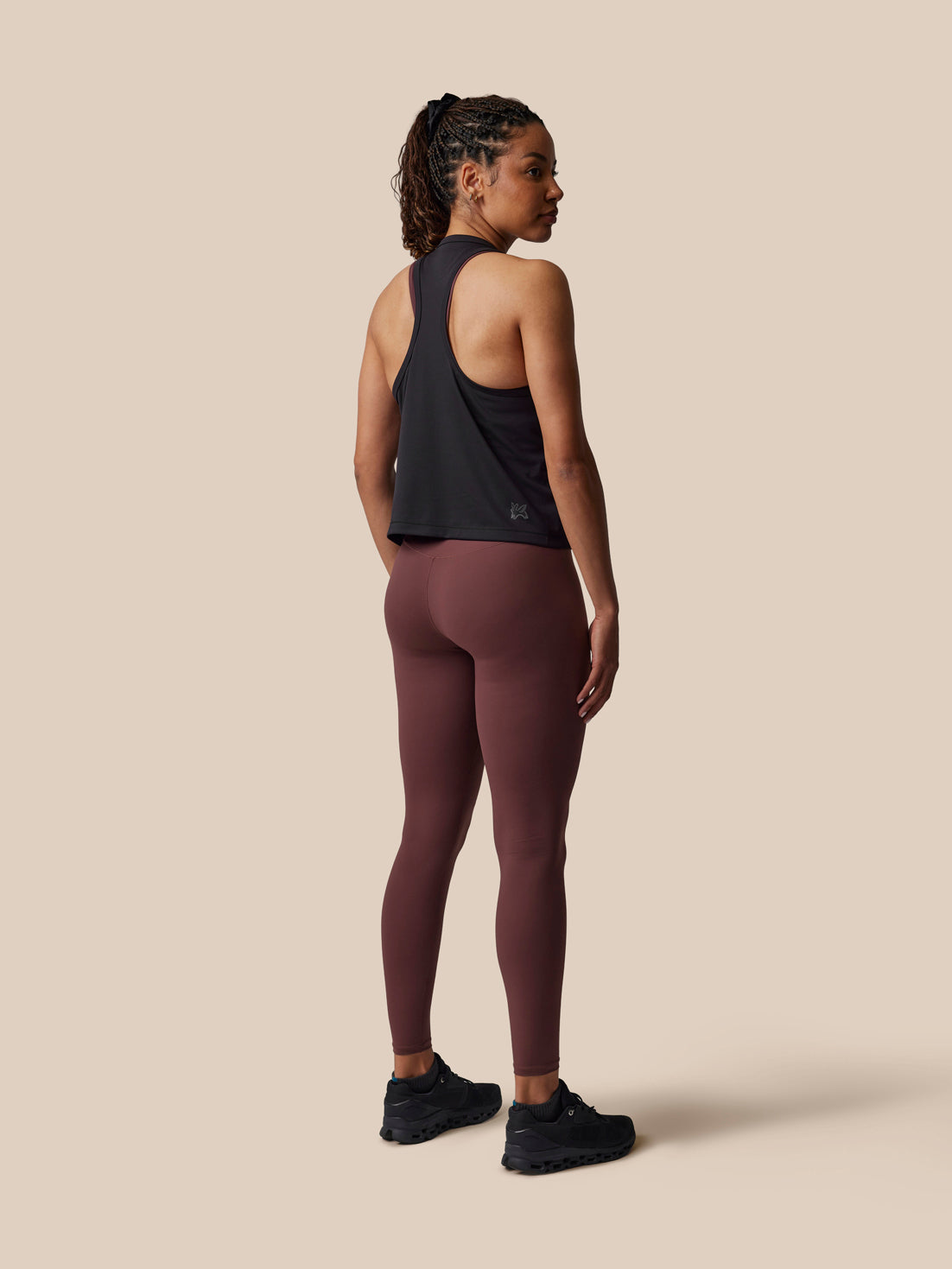 Person wearing a black tank top and maroon leggings on a beige background
