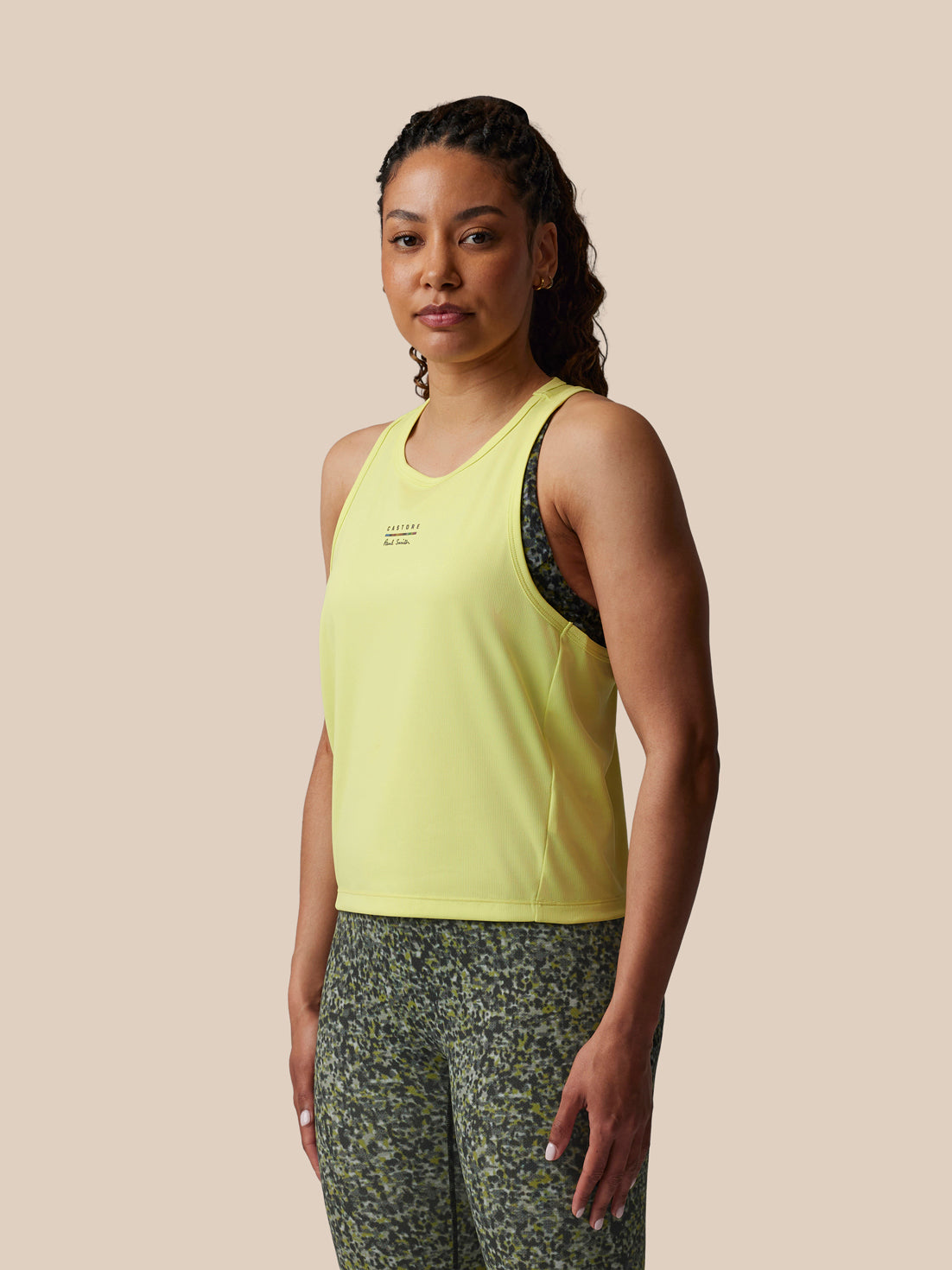 Woman wearing a yellow tank top and patterned pants on a beige background