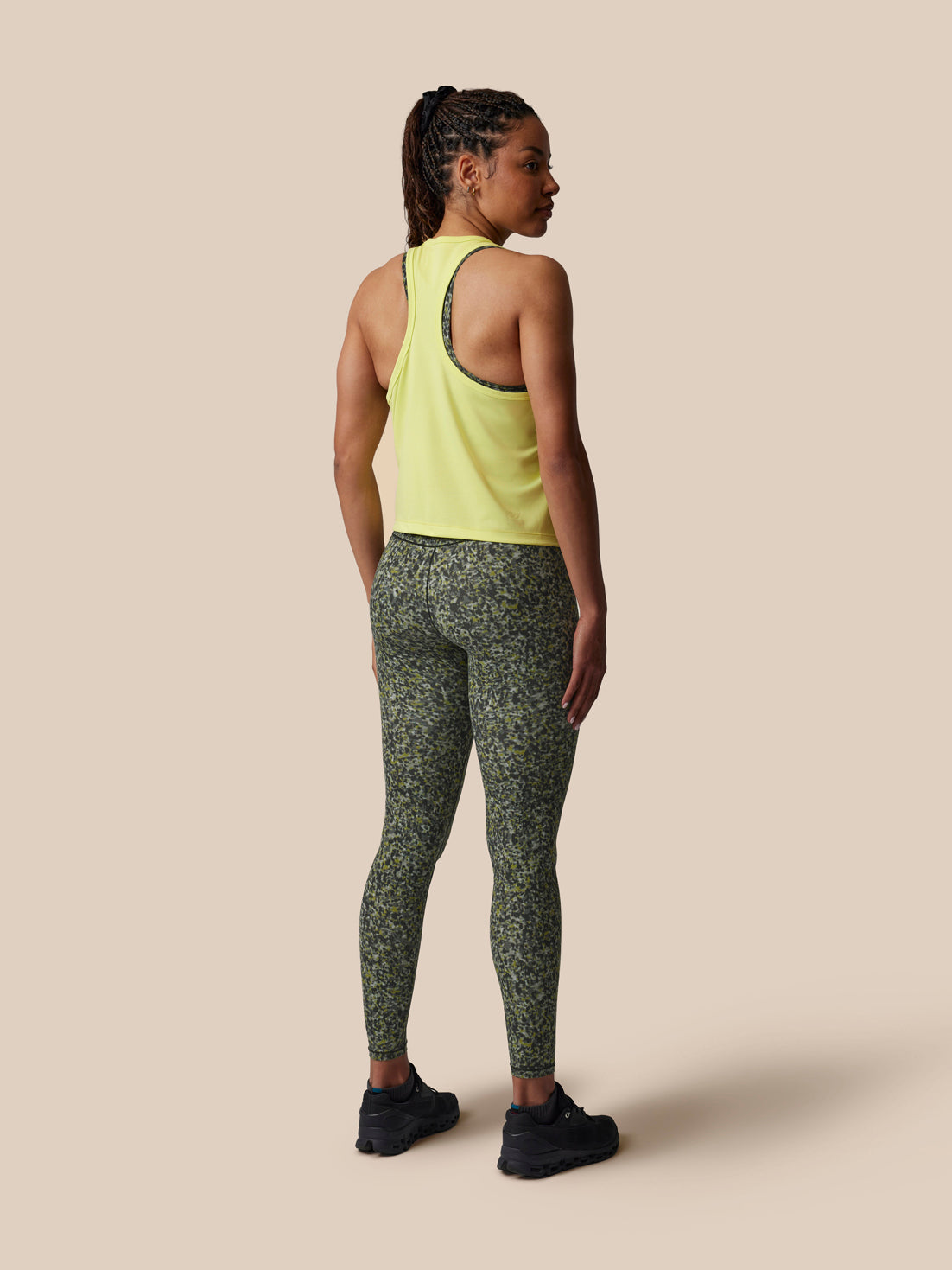 Woman wearing a light green tank top and patterned leggings on a beige background