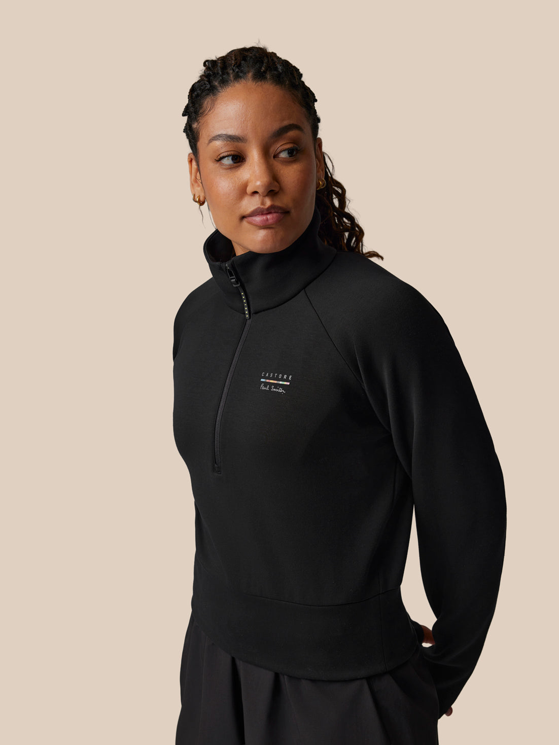 Person wearing a black quarter-zip sweatshirt with a logo on a beige background