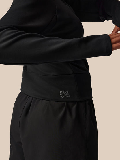 Person wearing a black outfit with a brand logo on a beige background