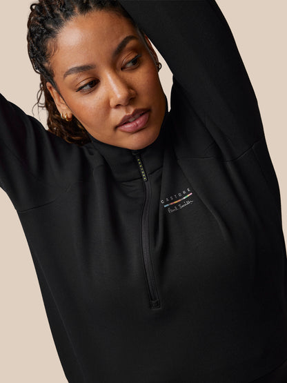 Person wearing a black quarter-zip sweatshirt with a brand logo on a beige background