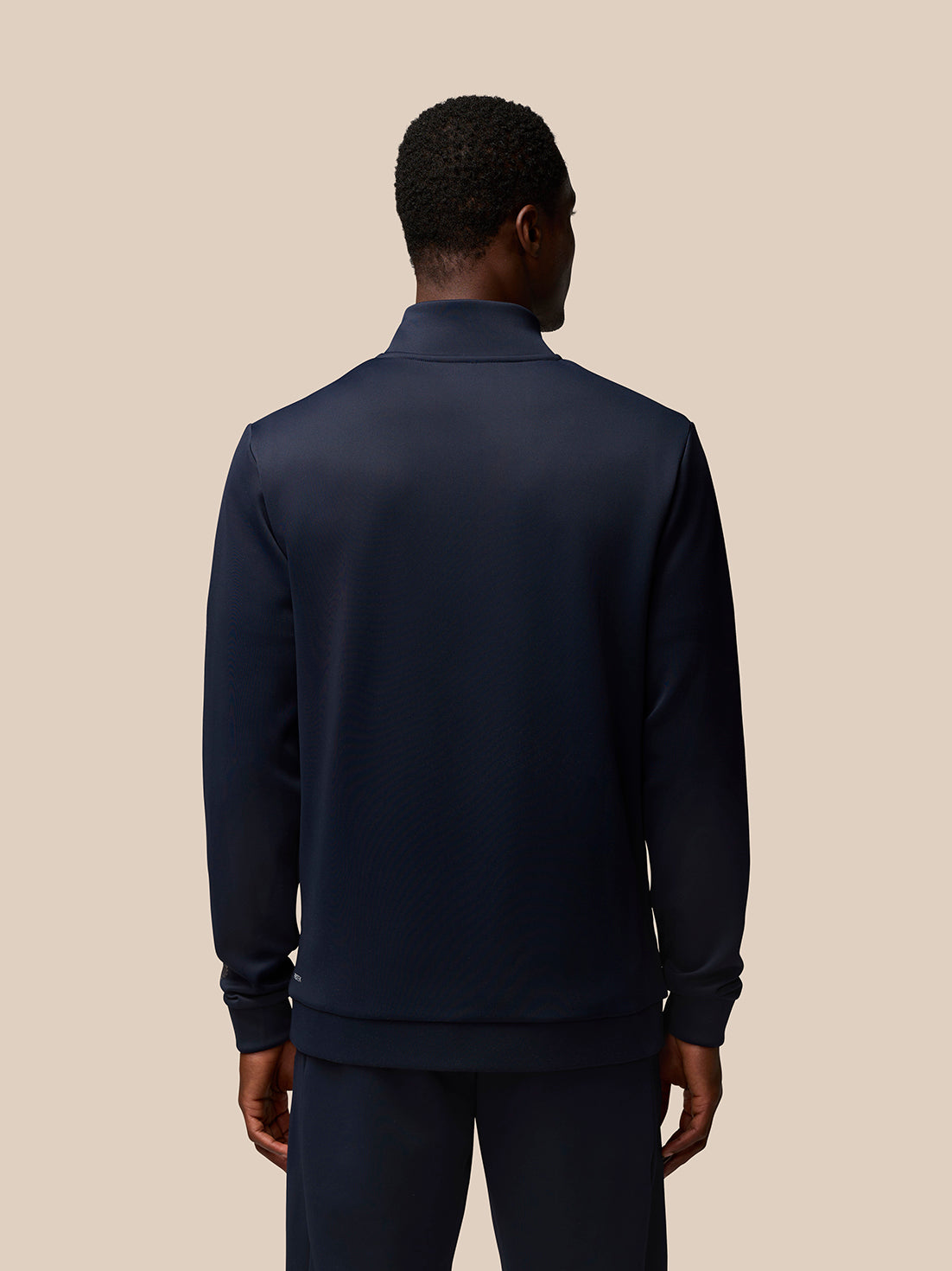 Rear view of male model wearing navy Castore Flex Lifestyle quarter-zip top.
