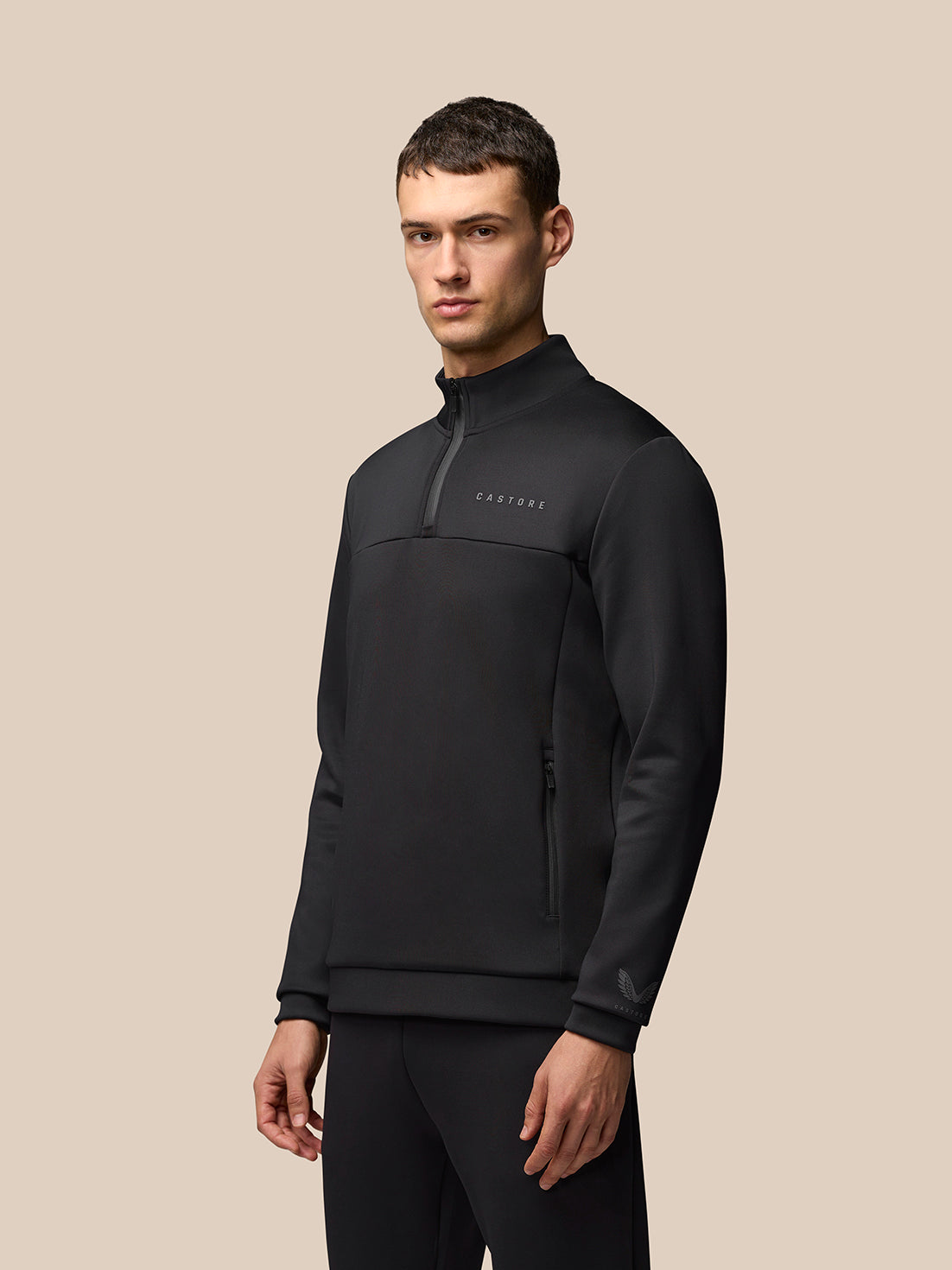 Male model wearing black Flex Quarter Zip Top with zip pockets and Castore branding on left chest left sleeve and left hem