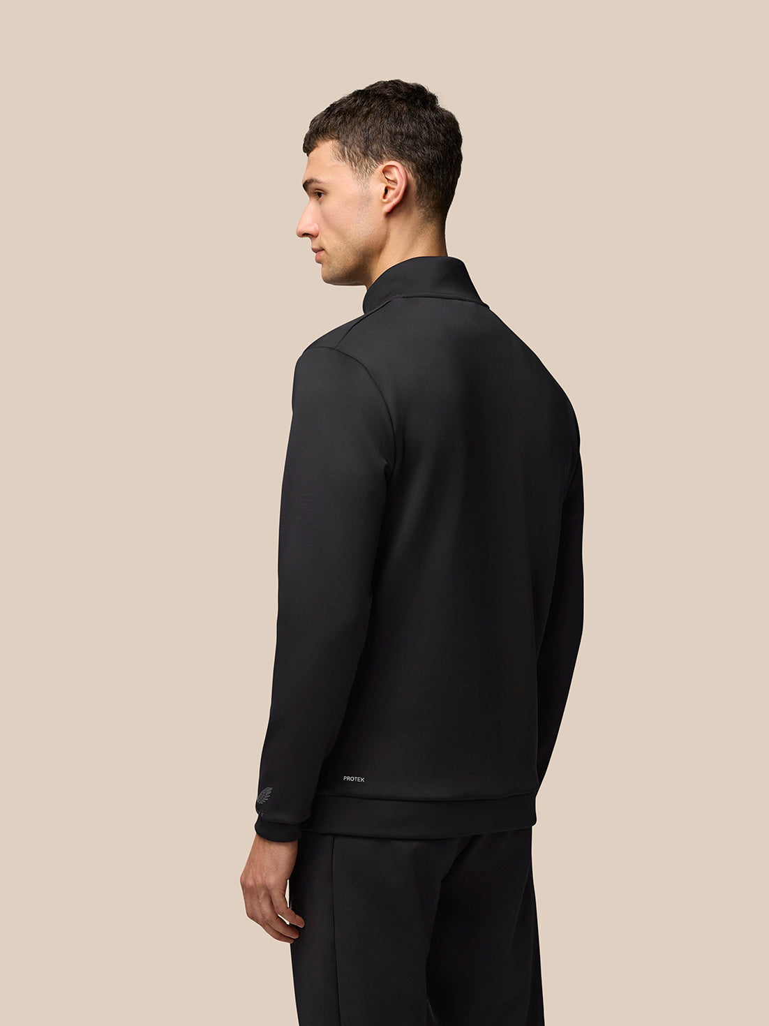 Back view of a man wearing black Flex Quarter Zip Top with a high collar and Protek branding at the lower back hem