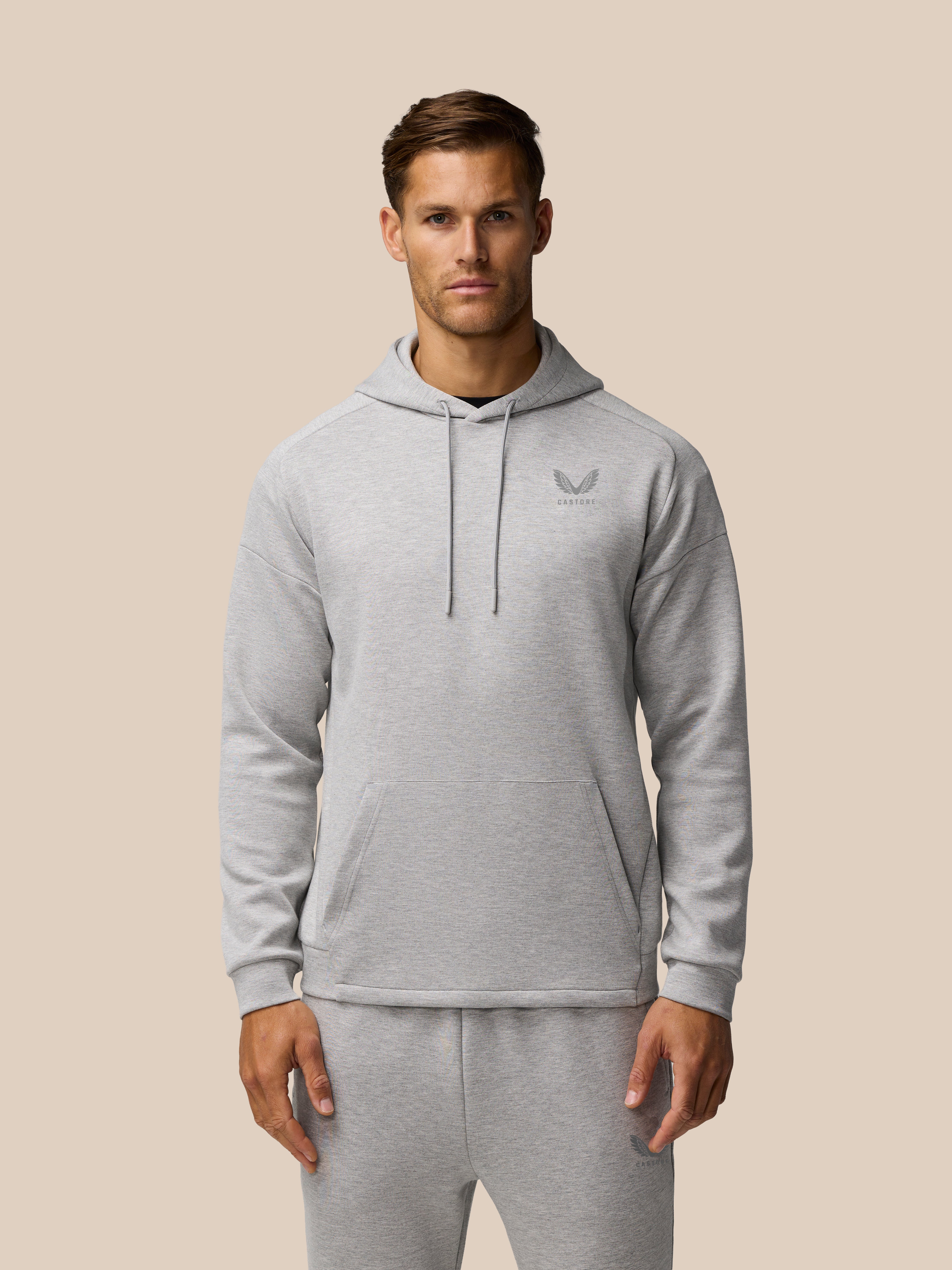 Front view of a man wearing a grey marl Travel Lifestyle Hoodie with three piece hood and left chest branding.