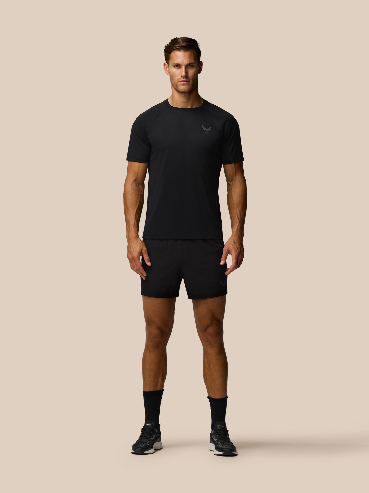 Man wearing a black athletic outfit with a brand logo on a beige background