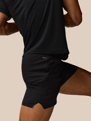 Person wearing black athletic shorts with a brand logo on a beige background
