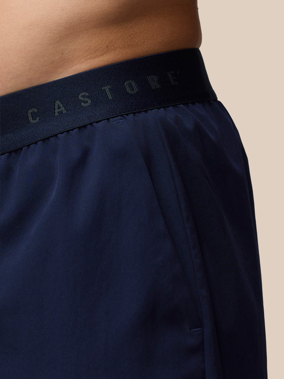 Navy blue shorts with 'Castore' waistband on a beige background