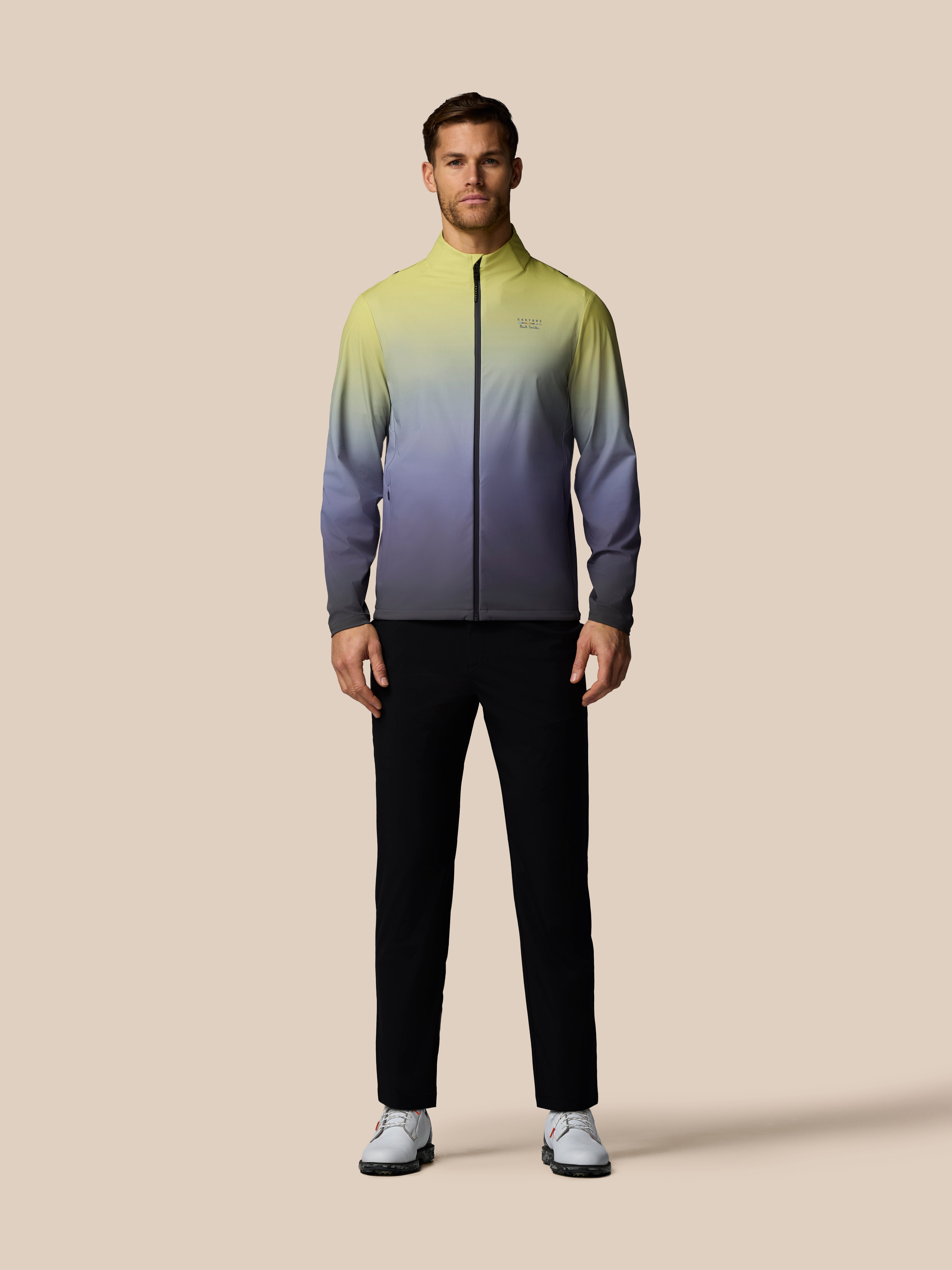 Man wearing a gradient jacket and black pants on a beige background