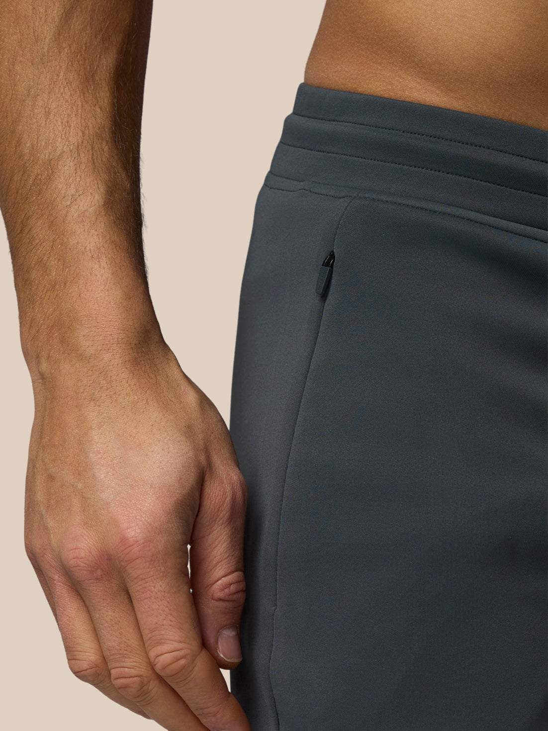 Close-up of a person wearing dark gray pants with a neutral background