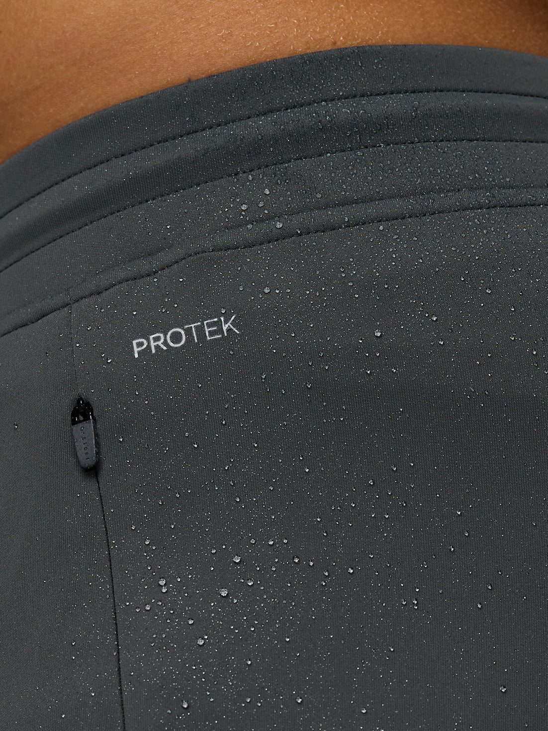 Close-up of grey joggers with 'PROTEK' branding on a light background