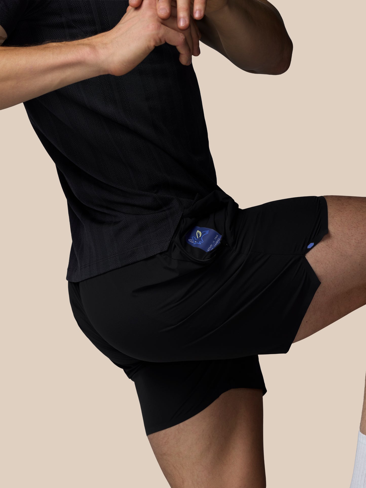Person wearing black shorts with a blue logo on a beige background