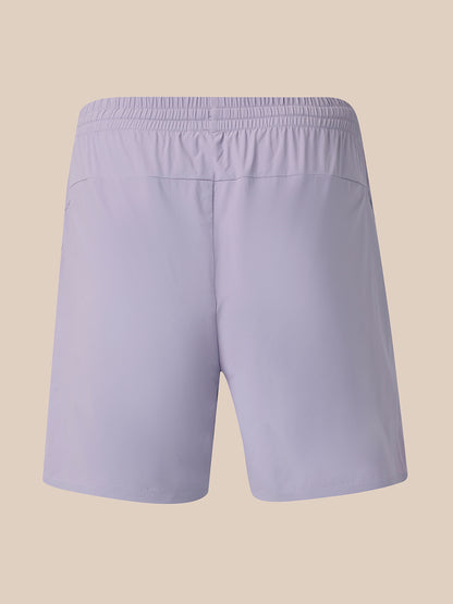 Light lavender athletic shorts with an elastic waistband, shown from the back on a solid beige background.