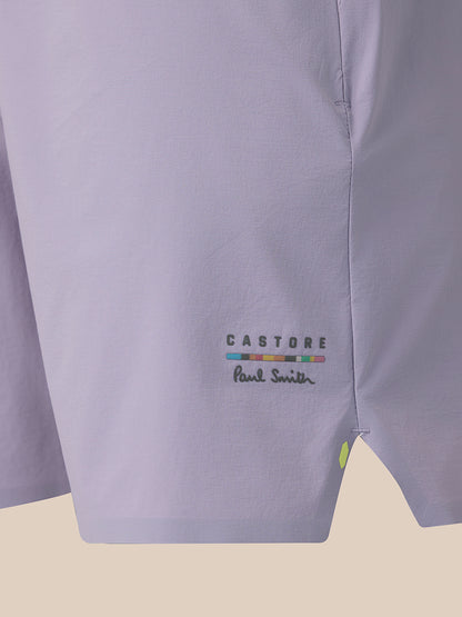 Close-up of a light lavender shirt fabric showing the 'CASTORE' and 'Paul Smith' logo embroidery on the lower left side, with a small lime green button detail.