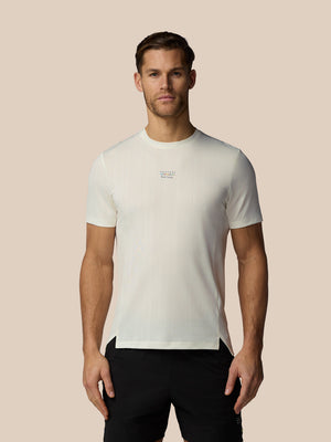 Man wearing a white t-shirt with a small logo on a beige background