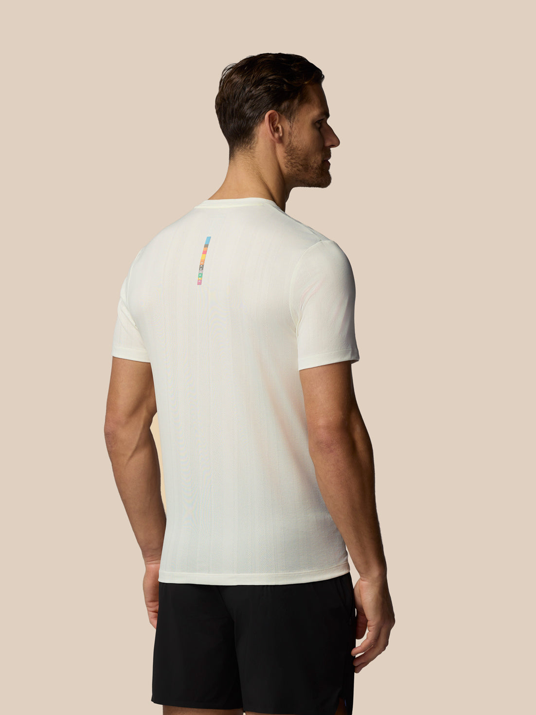 Man wearing a white t-shirt with a small logo on the back against a beige background