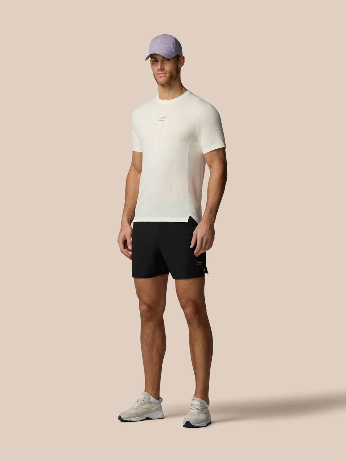 Man wearing a white t-shirt, black shorts, and a purple cap on a beige background